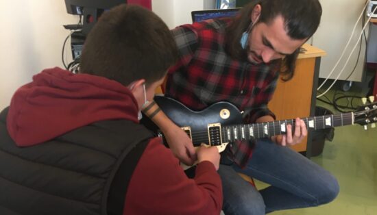 Un jeune élève fait bouger les cordes de la guitare tenue par Alvan