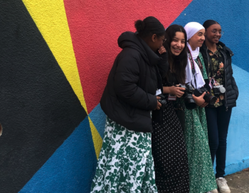 Quatre jeunes filles posent devant un mur coloré avec leurs appareils photos au tour du cou