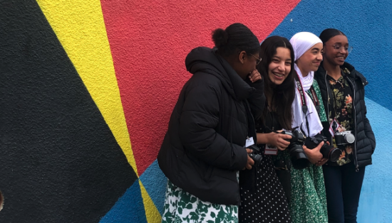 Quatre jeunes filles posent devant un mur coloré avec leurs appareils photos au tour du cou