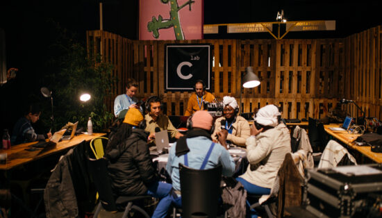 Photo de nuit en extérieur avec plusieurs personnes autours d'une table avec casques et micro. un homme est à une console son