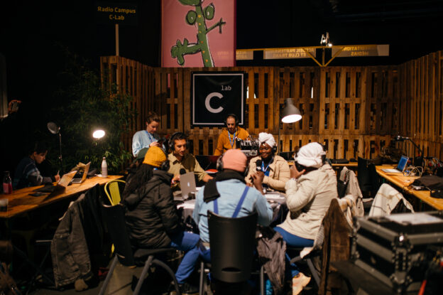Photo de nuit en extérieur avec plusieurs personnes autours d'une table avec casques et micro. un homme est à une console son