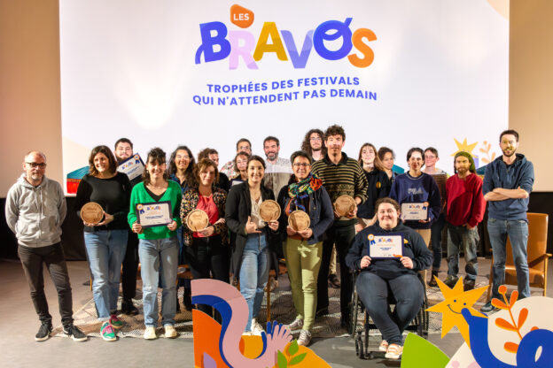 Vue d'ensemble de plusieurs personnes montrant leur diplôme ou trophée devant un grand écran "Bravos, trophées des festivals qui n'attendent pas demain"