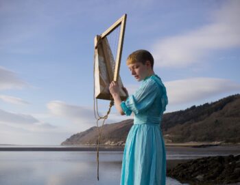 Photo d'une femme manipulant une sorte de harpe D.I.Y avec la mer, le ciel et une île en arrière plan