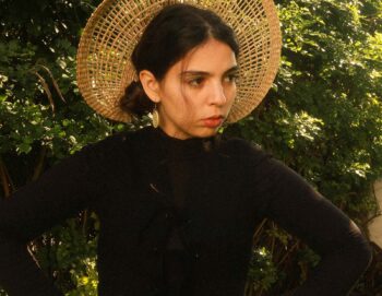 Portrait d'une femme avec un chapeau de paille ajouré posant devant un arbre