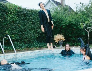 Photo assez floue de quatre hommes en costume dans une piscine dont un en plein saut