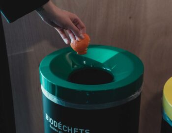 gros plan d'une main qui jette une pelure de mandarine dans une poubelle de biodéchets