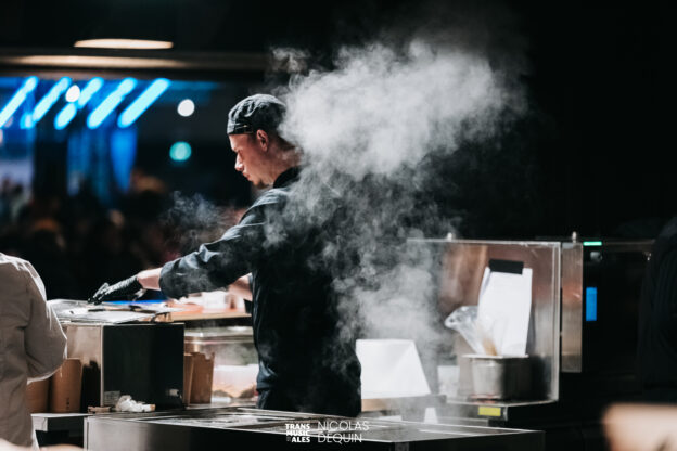 Vue d'un cuisinier de dos, il est en tenue noire, un nuage de vapeur monte derrière lui